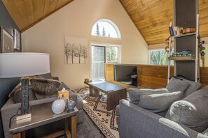 Ein gemütliches Wohnzimmer mit hoher Decke, Kamin, Fernseher und Bücherregal.