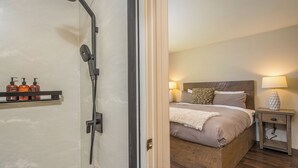 Ett hotellrum med dusch, en säng med sänggavel, sänglampor och en hylla med toalettartiklar.