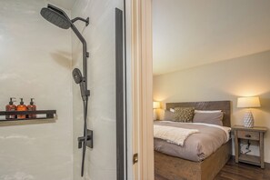 Ein Hotelzimmer mit Dusche, einem Bett mit Kopfteil, Nachttischlampen und einem Ablagefach mit Pflegeprodukten.