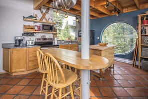 A kitchen with wooden cabinets, a central island, and a large window. - Between the Pines | Ski, Hike, Fish, Soak, Repeat (Big Sky)