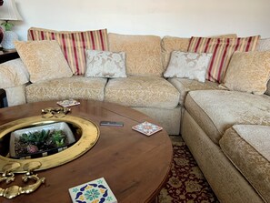 A beige sofa with patterned cushions, a wooden coffee table with a decorative bowl, and a patterned rug.