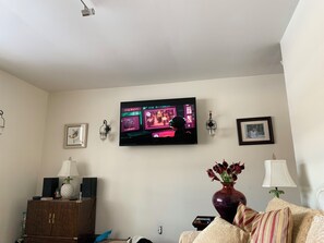 A living room with a flat-screen TV mounted on the wall, a wooden cabinet, a vase with flowers, and a sofa.