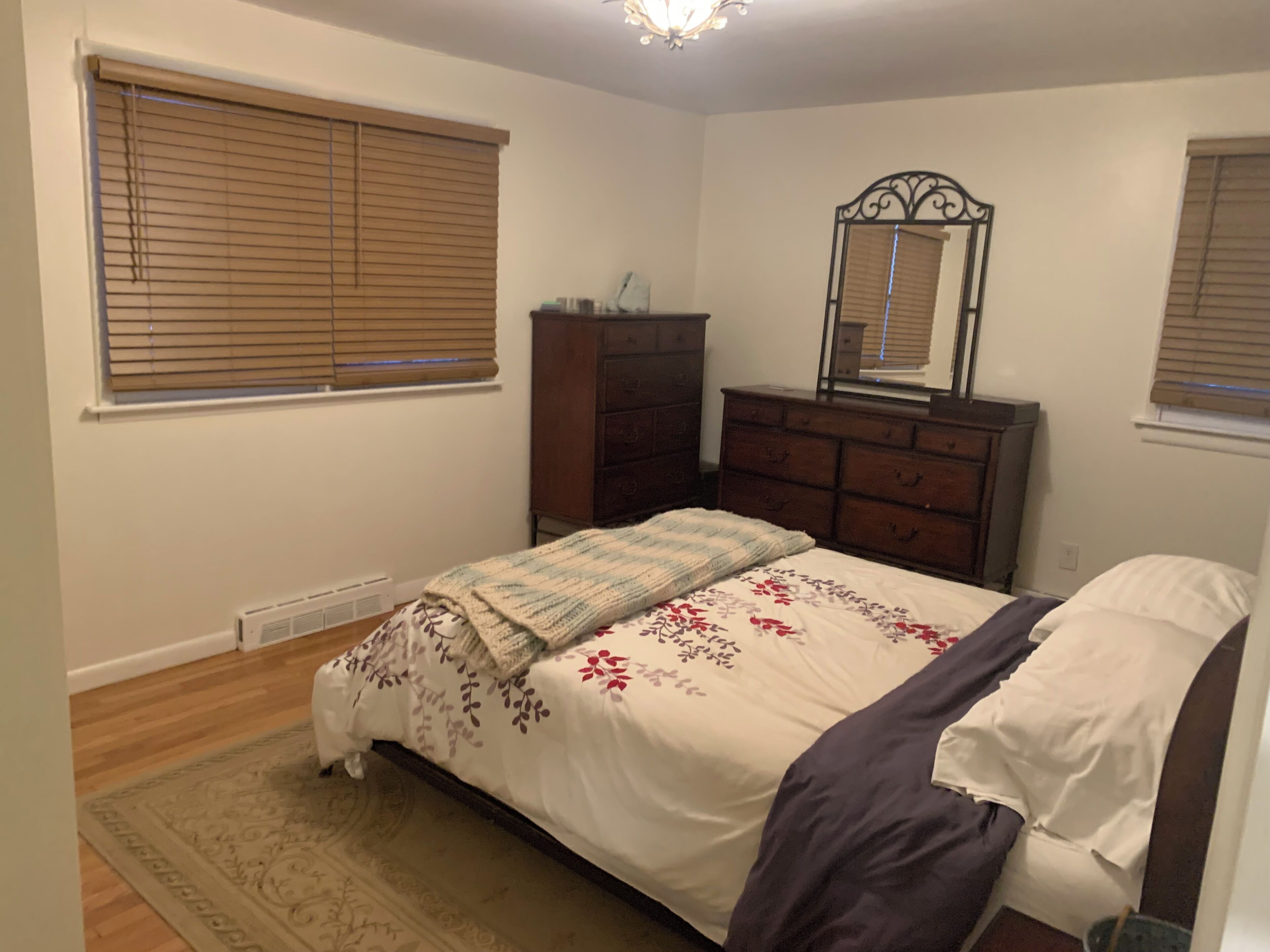 Un dormitorio con cama, cómoda, espejo y ventanas con persianas.