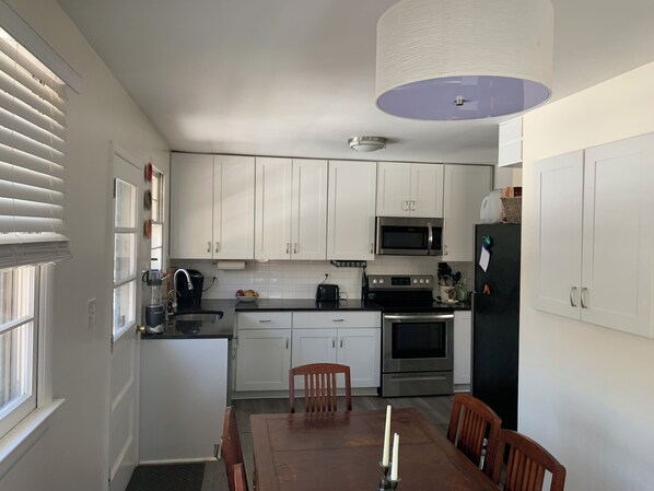 A modern kitchen with white cabinets, a microwave, stove, and a dining area with a table and chairs.