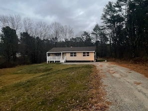 A single-story house with a front porch, surrounded by a wooded area.