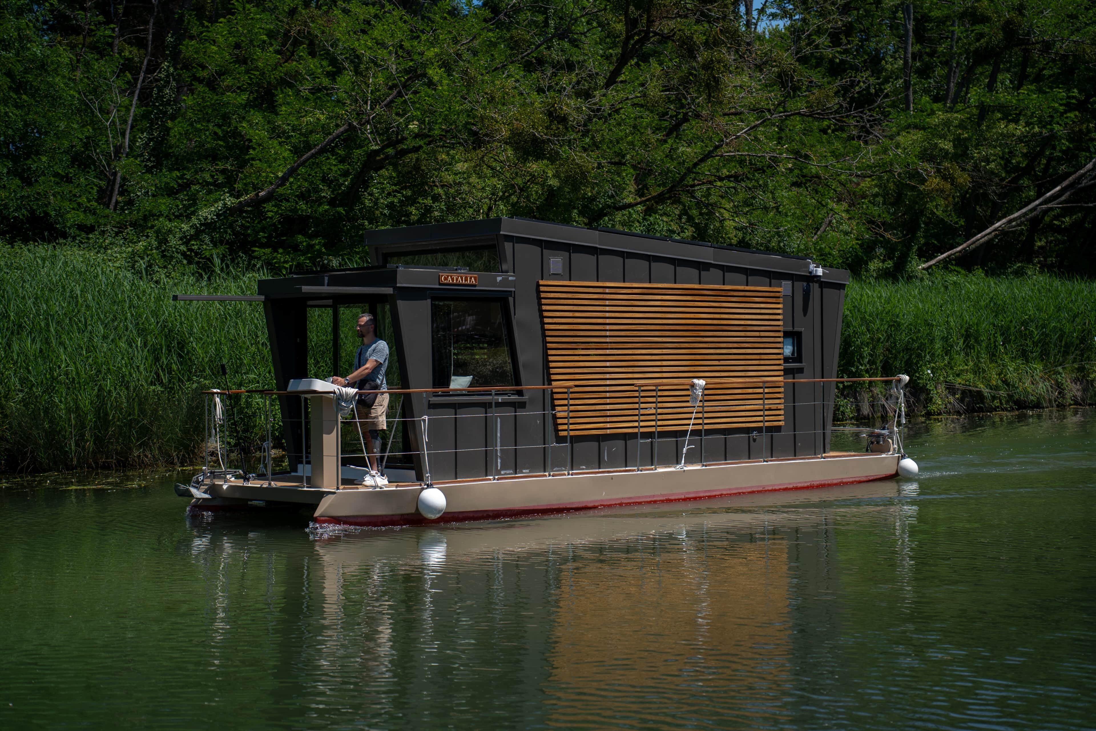 Une péniche dotée d’une terrasse, d’une petite cabine et d’une personne se tenant sur la terrasse.