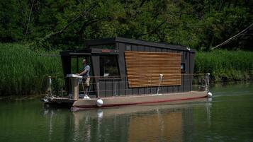 A houseboat with a deck area, a small cabin, and a person standing on the deck.