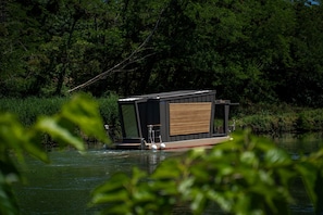 Una casa flotante de diseño moderno, ubicada en un cuerpo de agua rodeado de vegetación densa.