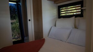 A bed with white linens, a red throw, and a window with blinds.