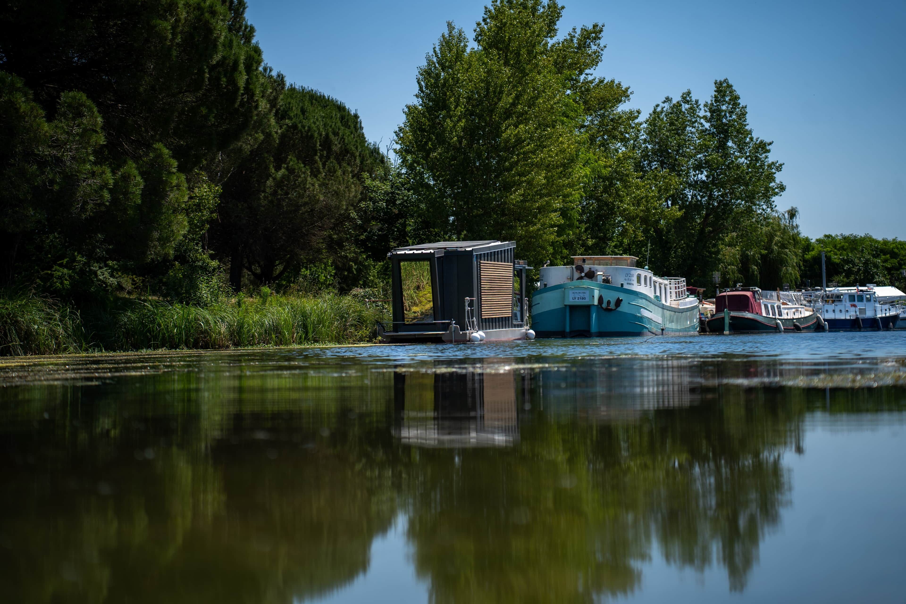 A calm river with boats docked, surrounded by dense trees.