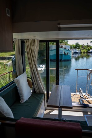 Un balcon avec un canapé vert, une petite table et une vue sur les bateaux qui naviguent.