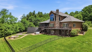 A two-story house with a large deck, a stone chimney, and a well-maintained lawn.
