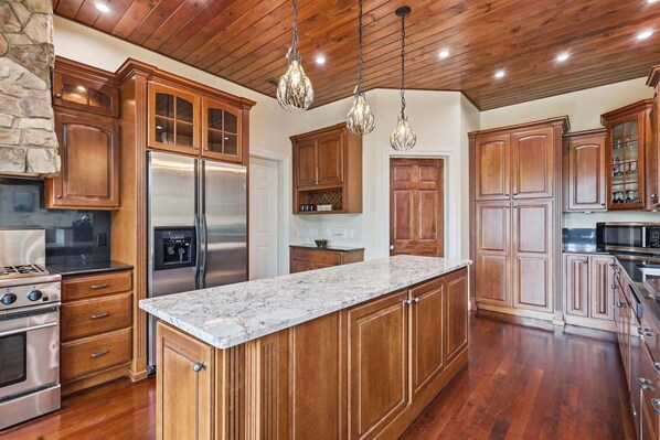 A kitchen with wooden cabinets, stainless steel appliances, a granite countertop, and a stone fireplace.