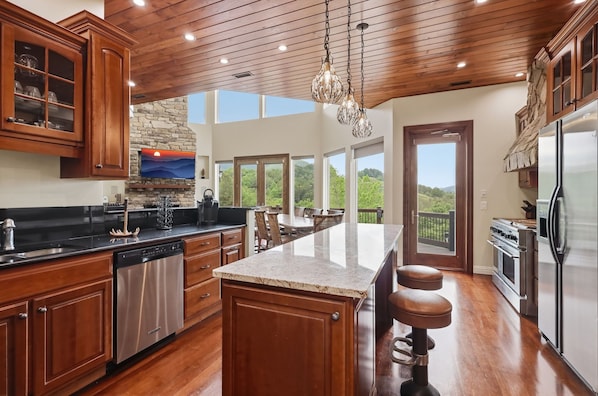 A spacious kitchen with wooden cabinets, a large island, stainless steel appliances, and a stone fireplace.