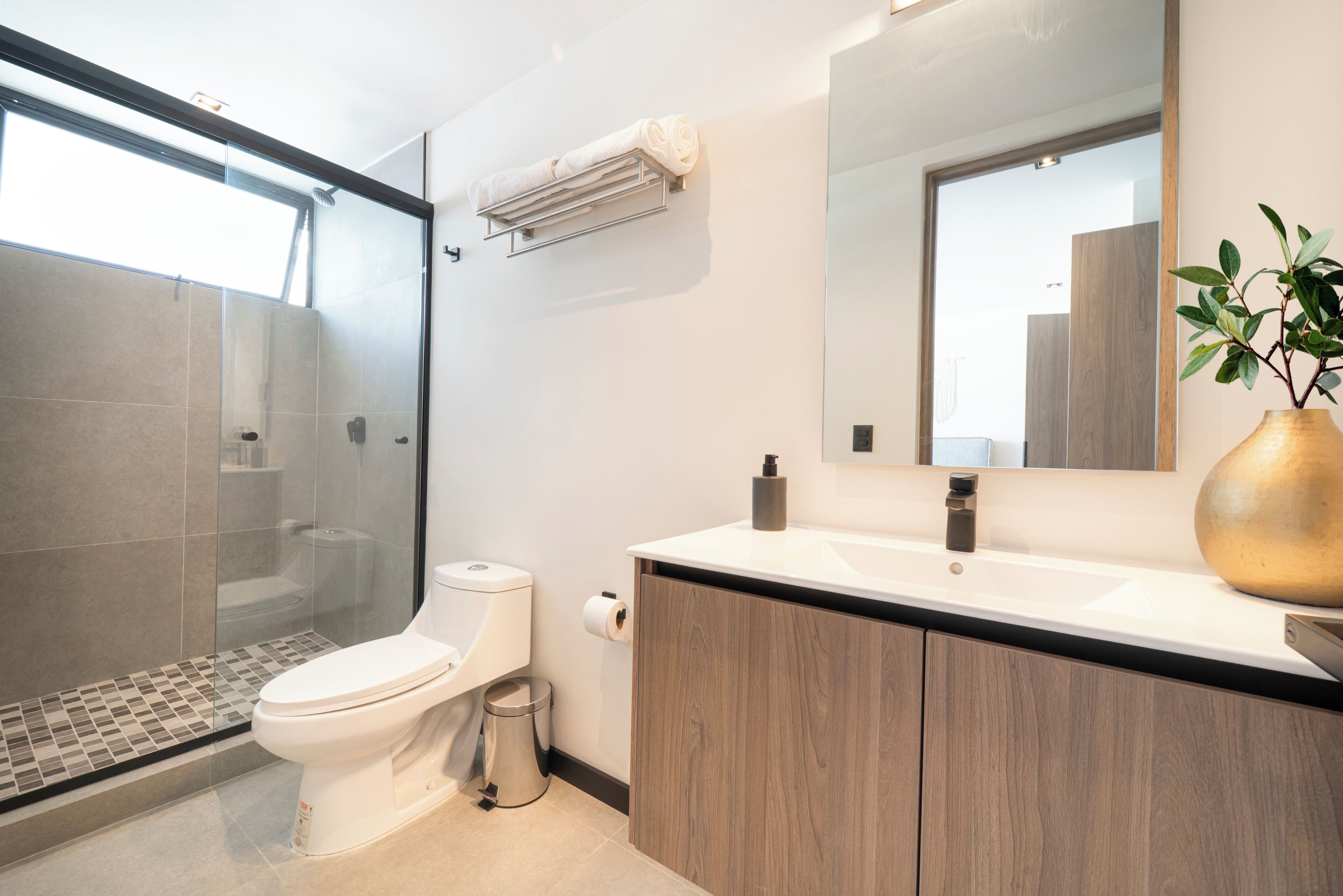 A modern bathroom with a glass shower enclosure, a white toilet, a wooden vanity, and a large mirror.