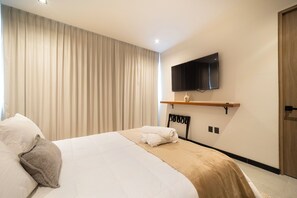 Ein Hotelzimmer mit Bett, Flachbildfernseher an der Wand, einer Holztür und einem Fenster mit Vorhängen.