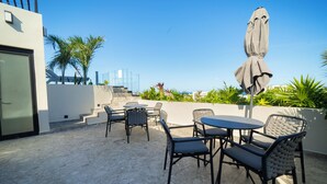 An outdoor patio with a table and chairs, a covered umbrella, and a staircase leading to an upper level. - Dept. Modern steps away from Quinta Av (Playa del Carmen)