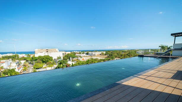 A swimming pool with a wooden deck, overlooking a cityscape and the sea. - Dept. Modern steps away from Quinta Av (Playa del Carmen)
