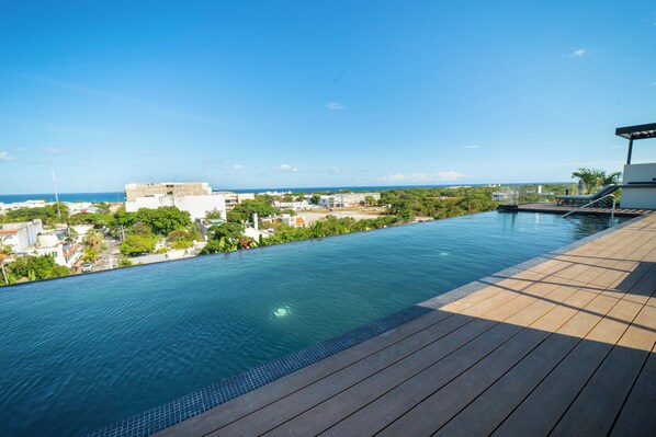 Ein Pool mit Holzterrasse, mit Blick auf eine Stadtlandschaft und das Meer.