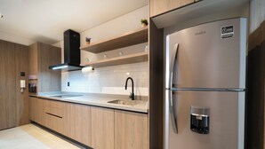 A modern kitchen with wooden cabinets, a stainless steel refrigerator, a built-in oven, and a sink with a black faucet. - Dept. Modern steps away from Quinta Av (Playa del Carmen)