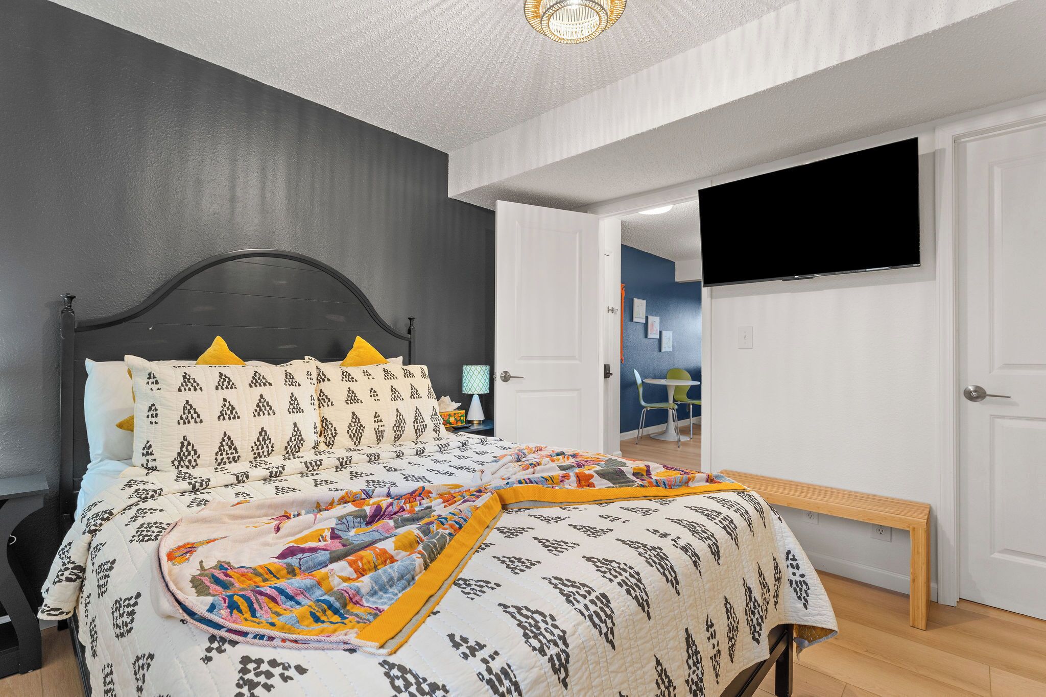 A bedroom with a bed, a bench, a TV, and a door leading to another room.