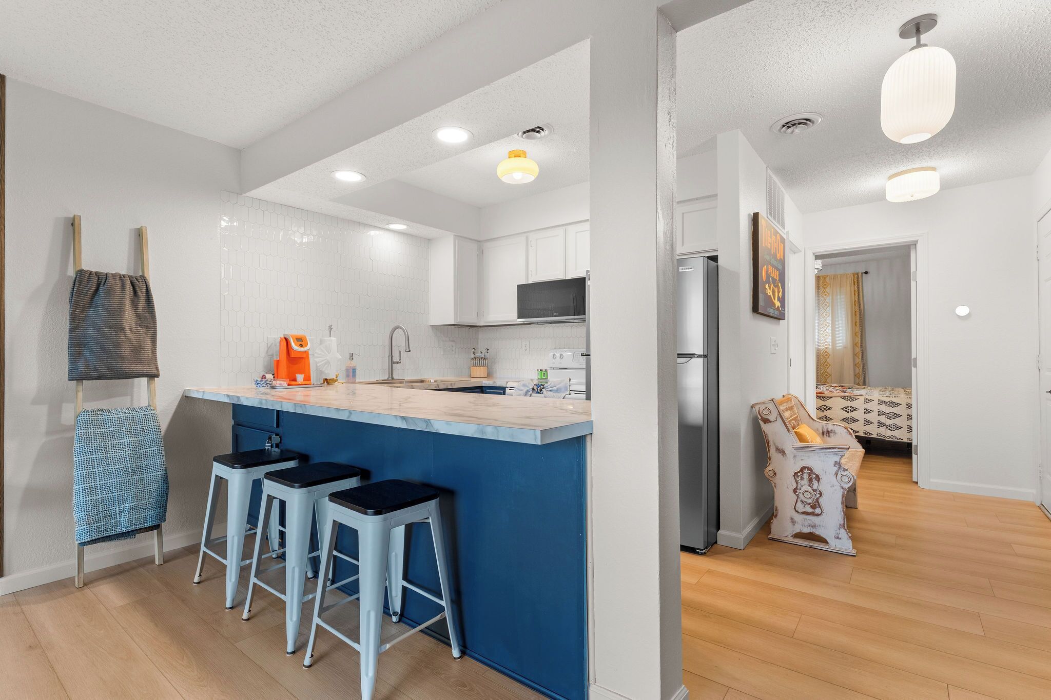 A modern kitchen with a central island, bar stools, and a dining area with a patterned sofa.