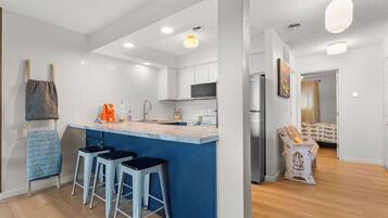 A modern kitchen with a central island, bar stools, and a dining area with a patterned sofa.