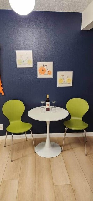 Een kamer met een ronde witte tafel, twee groene stoelen en drie kunstwerken in lijsten aan de muur.