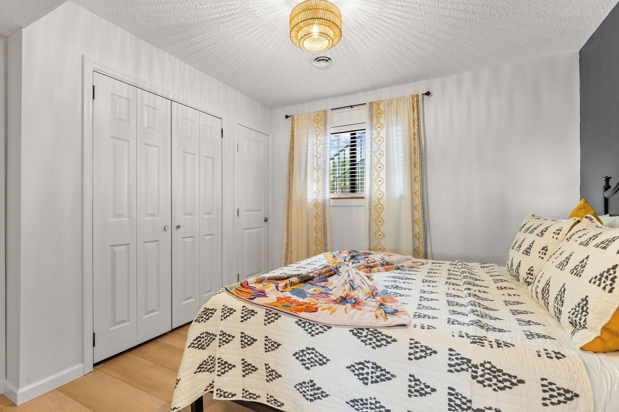 Un dormitorio con cama, armario, ventana con cortinas y una lámpara en el techo.