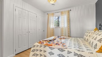 Een slaapkamer met een bed, een kledingkast, een raam met gordijnen en een plafondlamp.