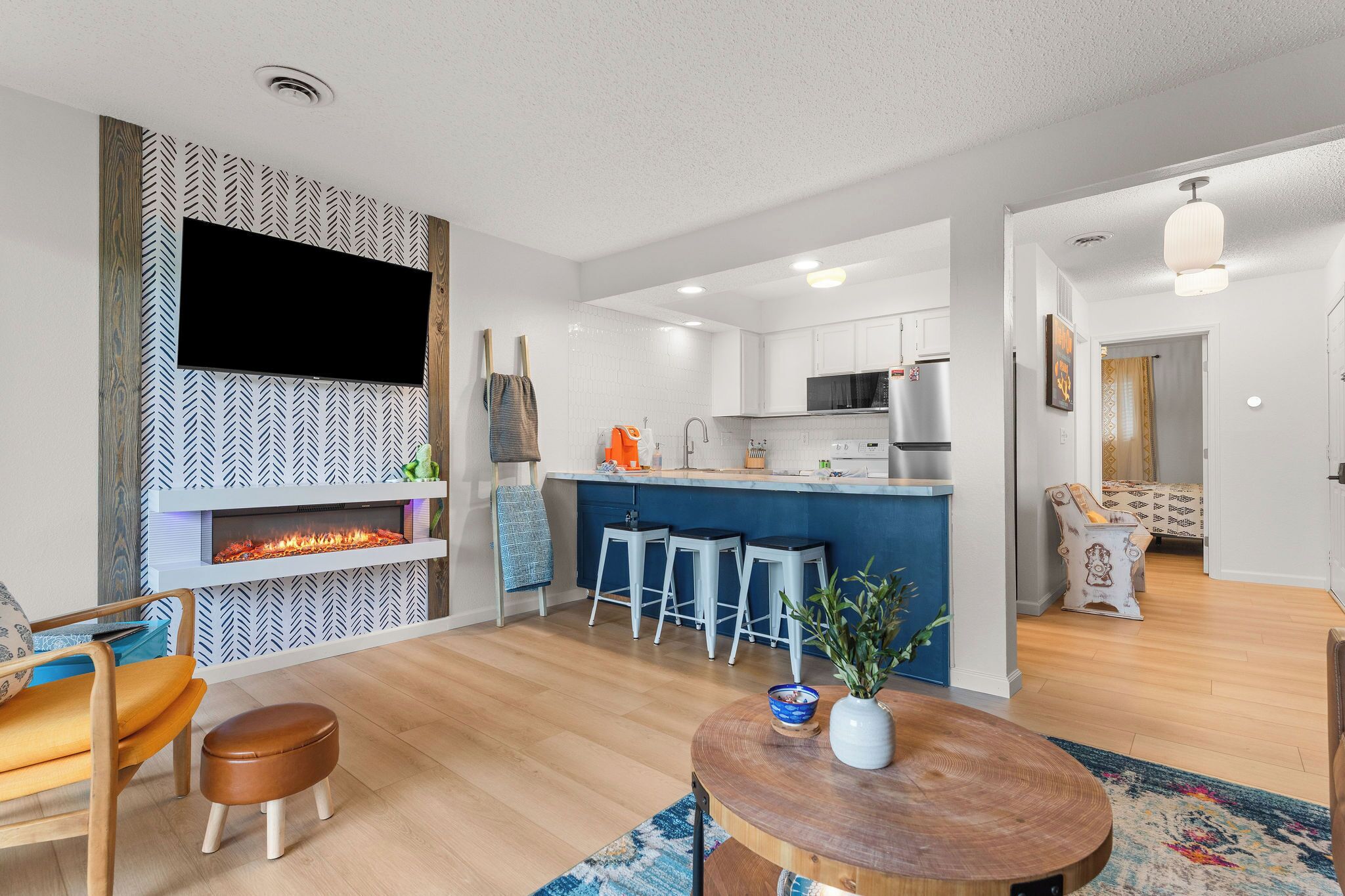 A modern kitchen with a flat-screen TV, a fireplace, and bar stools.