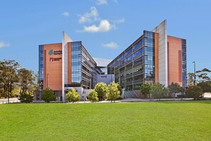 A modern building with a glass facade, labeled 'Macquarie University.' - A Little Slice of Paradise Pool, Gym+Parking (Macquarie Park)