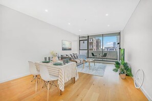 Een modern appartement met een eethoek, een bank, een salontafel en een balkon met uitzicht op de stad.