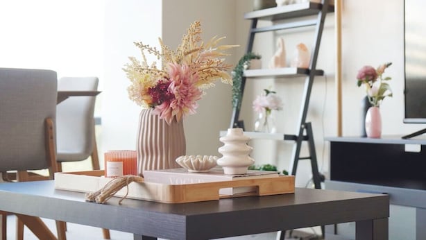 Un salon moderne avec une table en bois, un vase contenant des fleurs séchées, un livre et un bol décoratif.