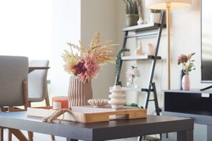 A modern living room with a wooden table, a vase with dried flowers, a book, and a decorative bowl.