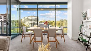 Un salon moderne doté d’un grand mur de verre, d’une table à manger avec quatre chaises et d’une étagère décorative agrémentée de plantes.