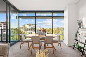Ein modernes Wohnzimmer mit einer großen Glasswand, einem Esstisch mit vier Stühlen und einem dekorativen Regal mit Pflanzen.