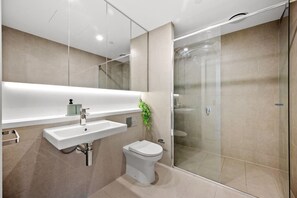 Un baño moderno con cabina de ducha de vidrio, un lavamanos blanco y un inodoro.