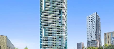 A modern high-rise building with a curved facade, surrounded by other buildings and a clear sky.