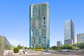 Un moderno edificio de gran altura con fachada curva, rodeado de otros edificios y un cielo despejado.