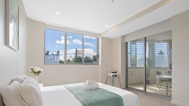 Een slaapkamer met een bed, een raam met uitzicht, een stoel en een balkon.