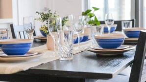 Een eettafel gedekt met blauwe kommen, glazen en een vaas met groene planten.