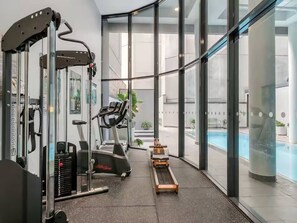 A gym with exercise equipment, a treadmill, and a pool visible through large windows. - Surry Hills Chic 1BR in Prime Dining & City Spots (Surry Hills)