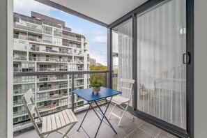 A balcony with a table and chairs, a potted plant, and a view of a multi-story building. - Surry Hills Chic 1BR in Prime Dining & City Spots (Surry Hills)