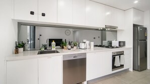 A modern kitchen with white cabinets, a dishwasher, a stove, a microwave, and a refrigerator. - Designer 1BR Apt | Rooftop Oasis & Fast CBD Access (Rosebery)