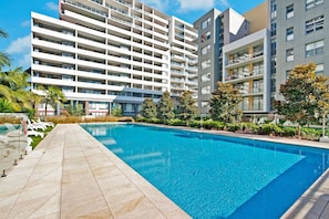Une piscine à l’eau d’un bleu limpide, entourée d’une allée dallée.