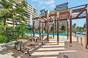 A rooftop pool area with wooden pergolas, lounge chairs, and a swimming pool. - Elegant Loft Living w/ Soaring Ceilings (Macquarie Park)