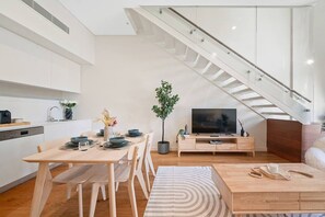 A modern living space with a dining area, a TV, a staircase, and a kitchen. - Elegant Loft Living w/ Soaring Ceilings (Macquarie Park)