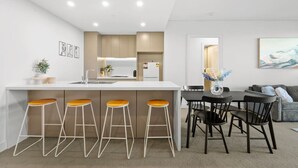 A modern kitchen with a central island, bar stools, a dining table with chairs, and a living area with a couch and artwork.