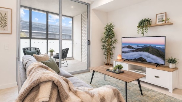 En moderne stue med sofa, fjernsyn og balkon med udsigt.